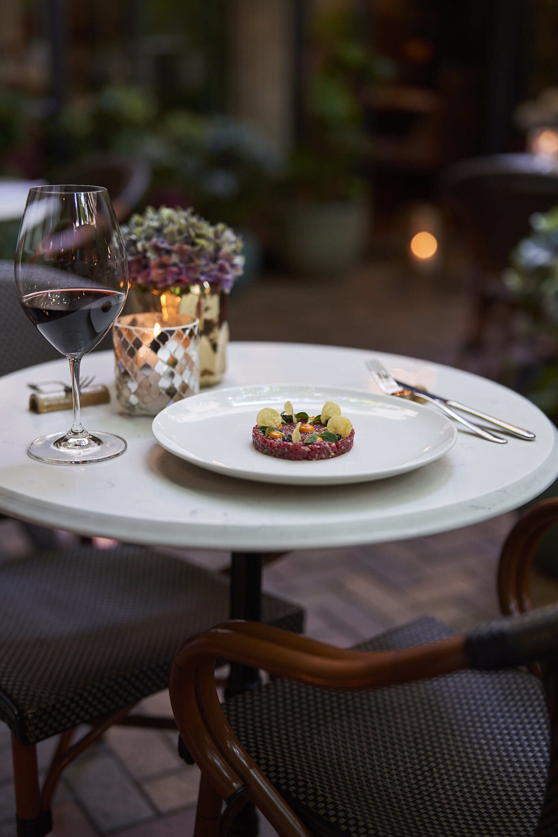 Une table à manger avec une assiette de nourriture, un verre de vin rouge et une bougie.