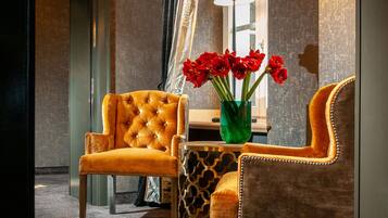 A hotel room with a tufted armchair, a side table with a vase of red flowers, and a patterned rug.