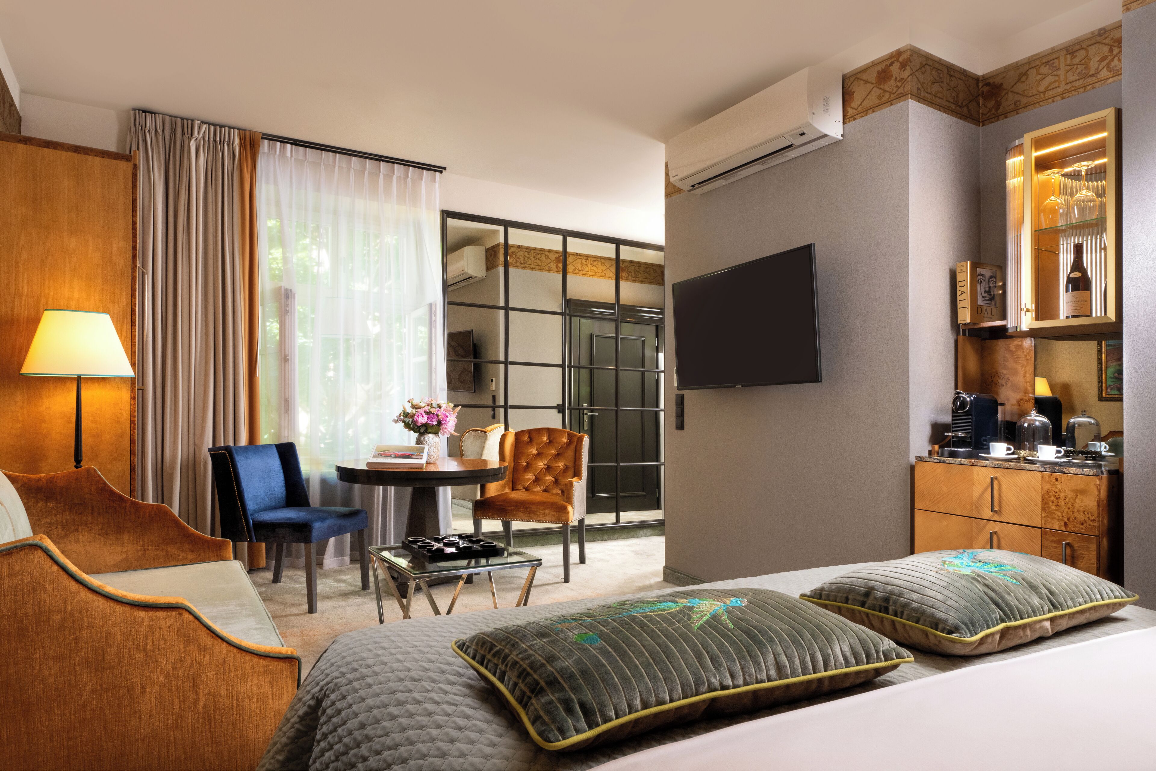 A hotel room with a bed, a desk, a chair, a TV, and a minibar.