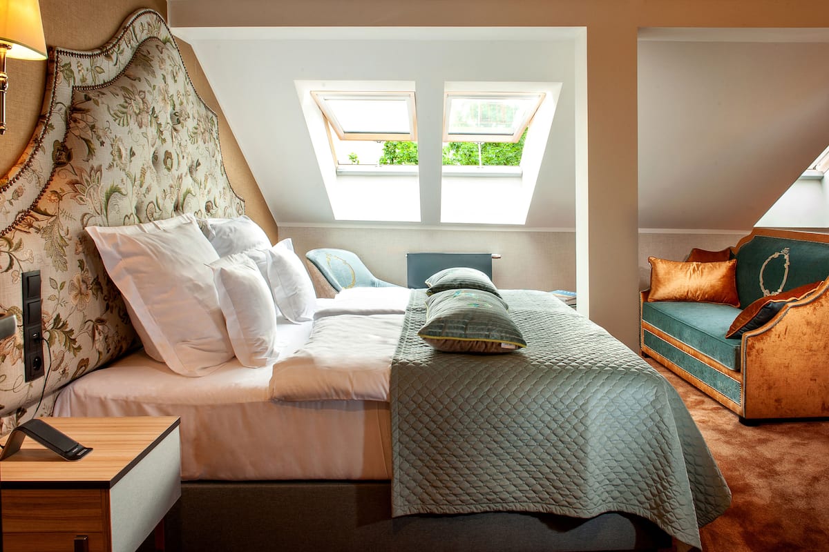 A bedroom with a bed, a bedside table, a lamp, a window, and a sofa.