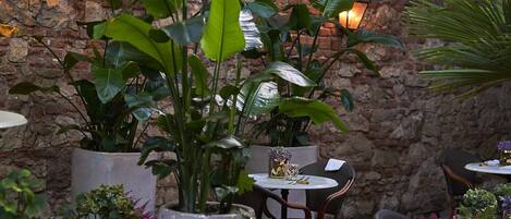 An outdoor patio with brick walls, potted plants, and tables with chairs.