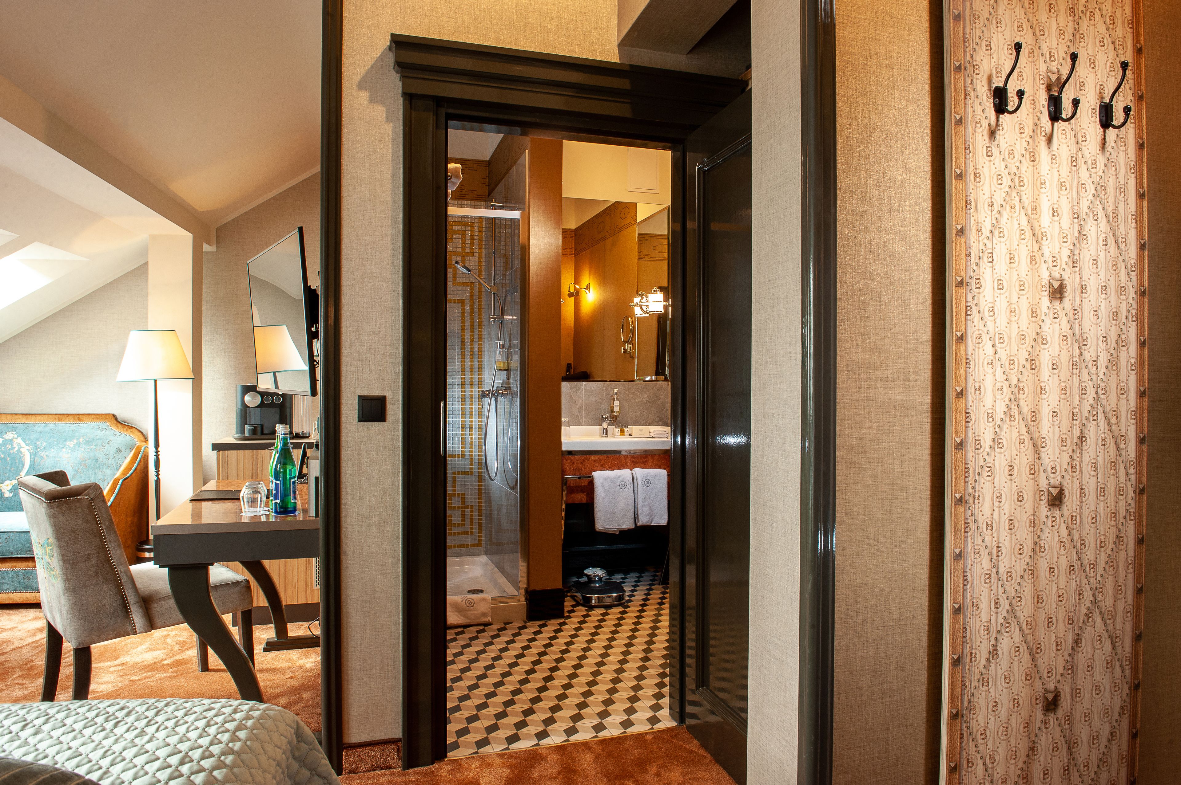 A hotel room with a bed, a desk with a lamp, a bathroom with a shower, and a patterned wall.