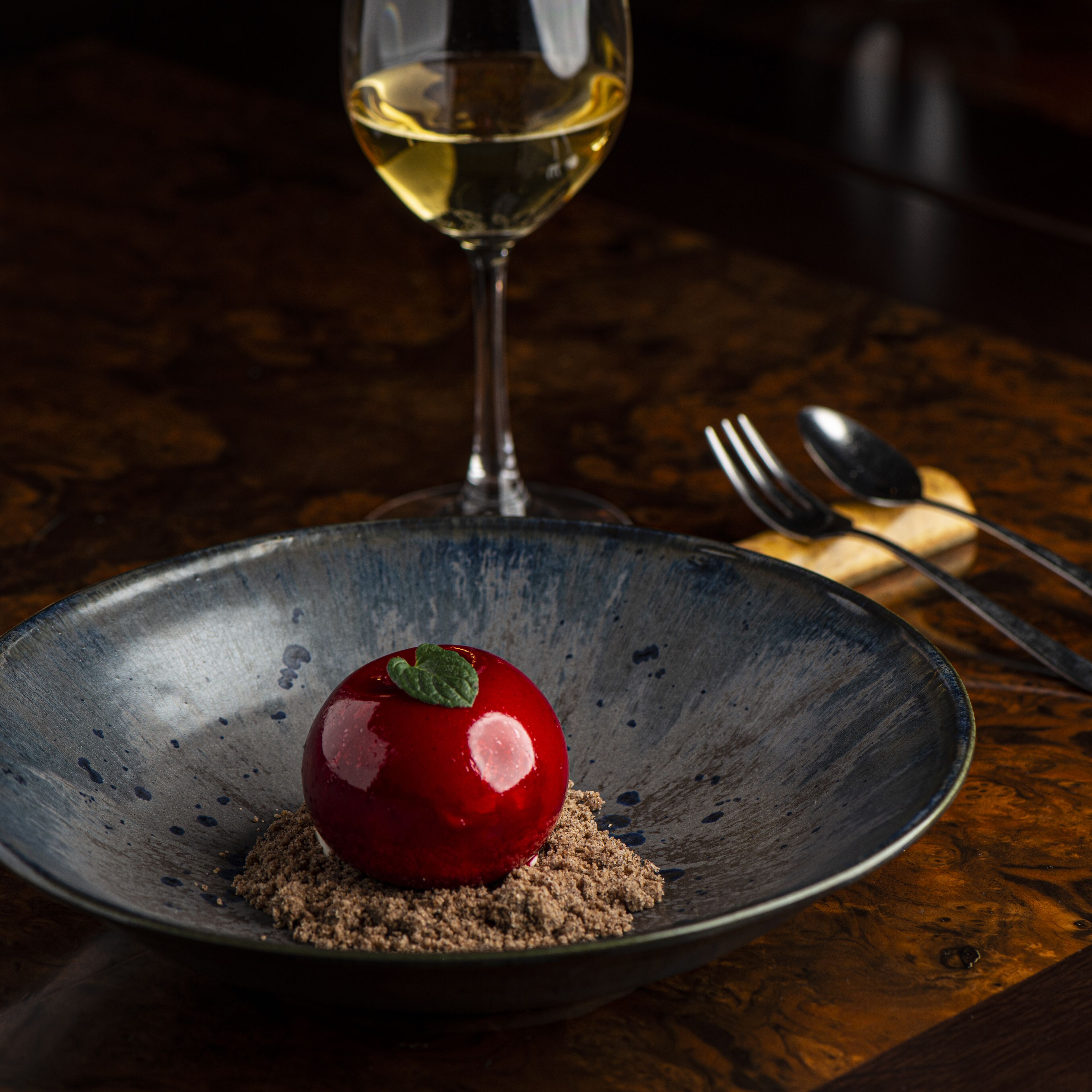 Un dessert présenté sur une assiette, avec un verre à vin en arrière-plan.