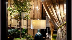Une pièce avec une grande fenêtre, une plante en pot, une lampe et un rideau.