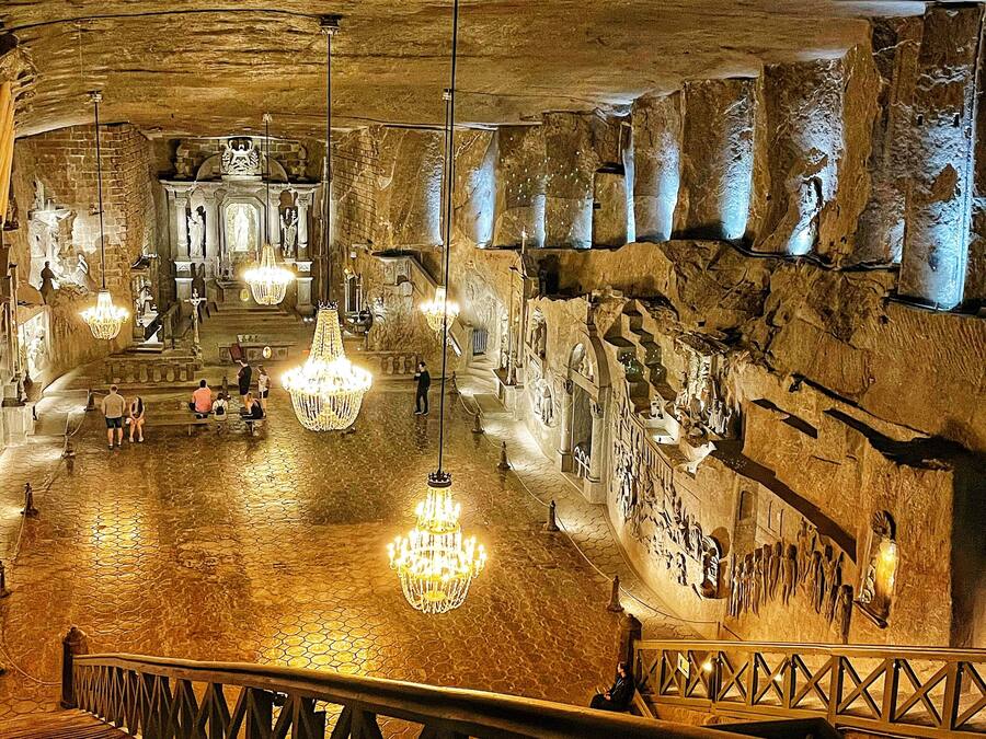 A spacious underground chamber with stone walls, a central altar, and chandeliers.
