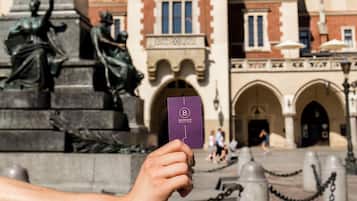 A hand holding a purple card in front of a statue and a building with arched windows and a domed roof.