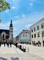 A historic square with a prominent tower, cobblestone pavement, and classical architecture.