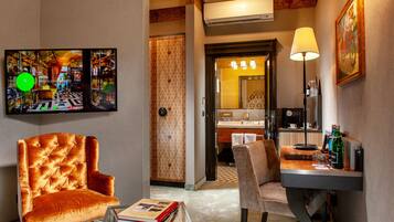 Une chambre d’hôtel dotée d’un grand téléviseur à écran plat, d’un fauteuil capitonné, d’une petite table avec un livre, d’un bureau avec une lampe et d’une salle de bain visible à travers une porte ouverte.