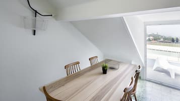 A dining area with a long wooden table, four chairs, a small potted plant, and a wire basket on the wall.