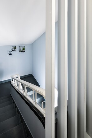 A modern staircase with a black handrail and white balusters, leading to a landing with a light blue wall and three small framed pictures.