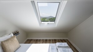 A bedroom with a skylight, a bed with white linens, a patterned pillow, and a small shelf with candles. - JR Studios & Suites (Coimbra)