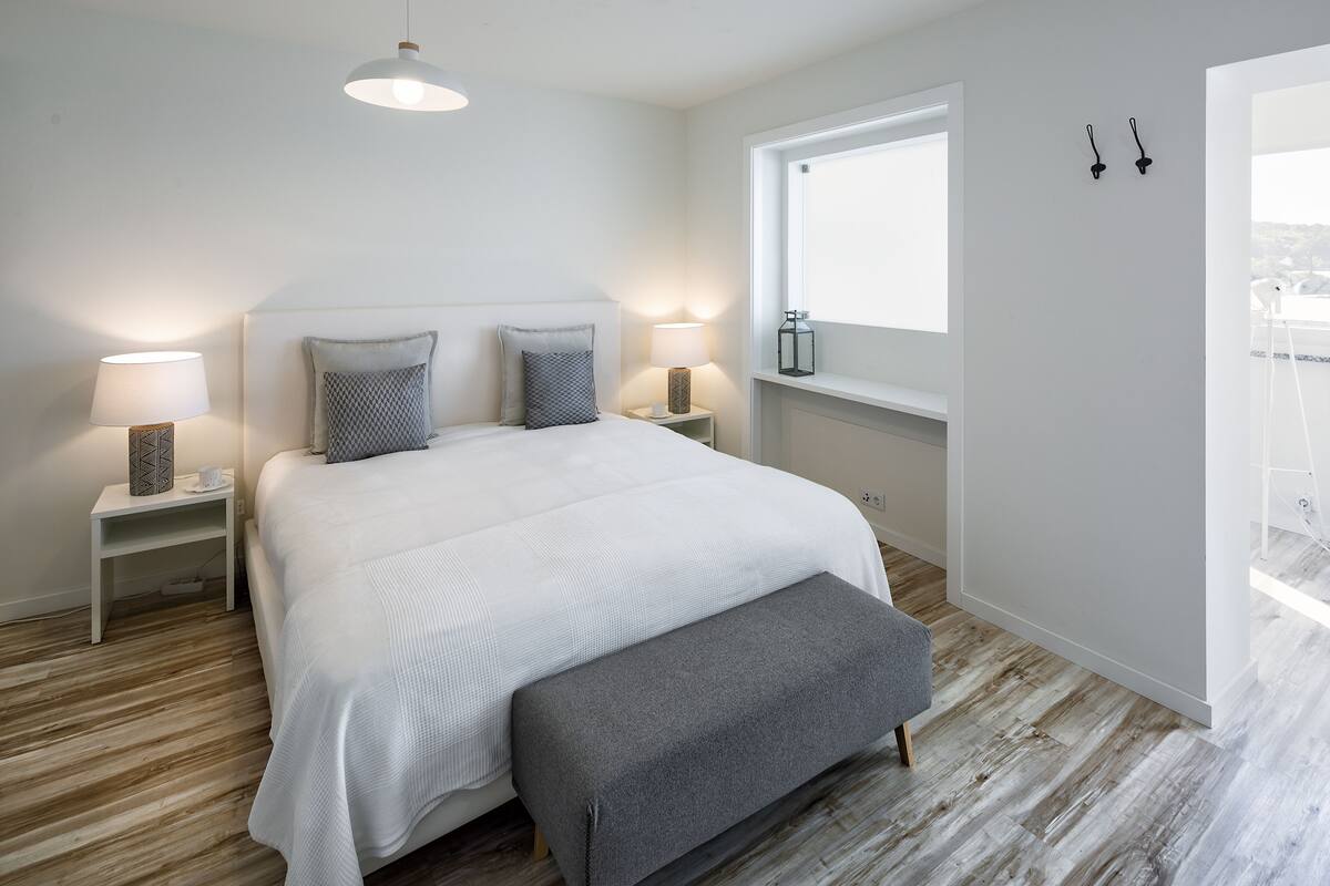 A bedroom with a large bed, bedside lamps, a window, and a view of the city.