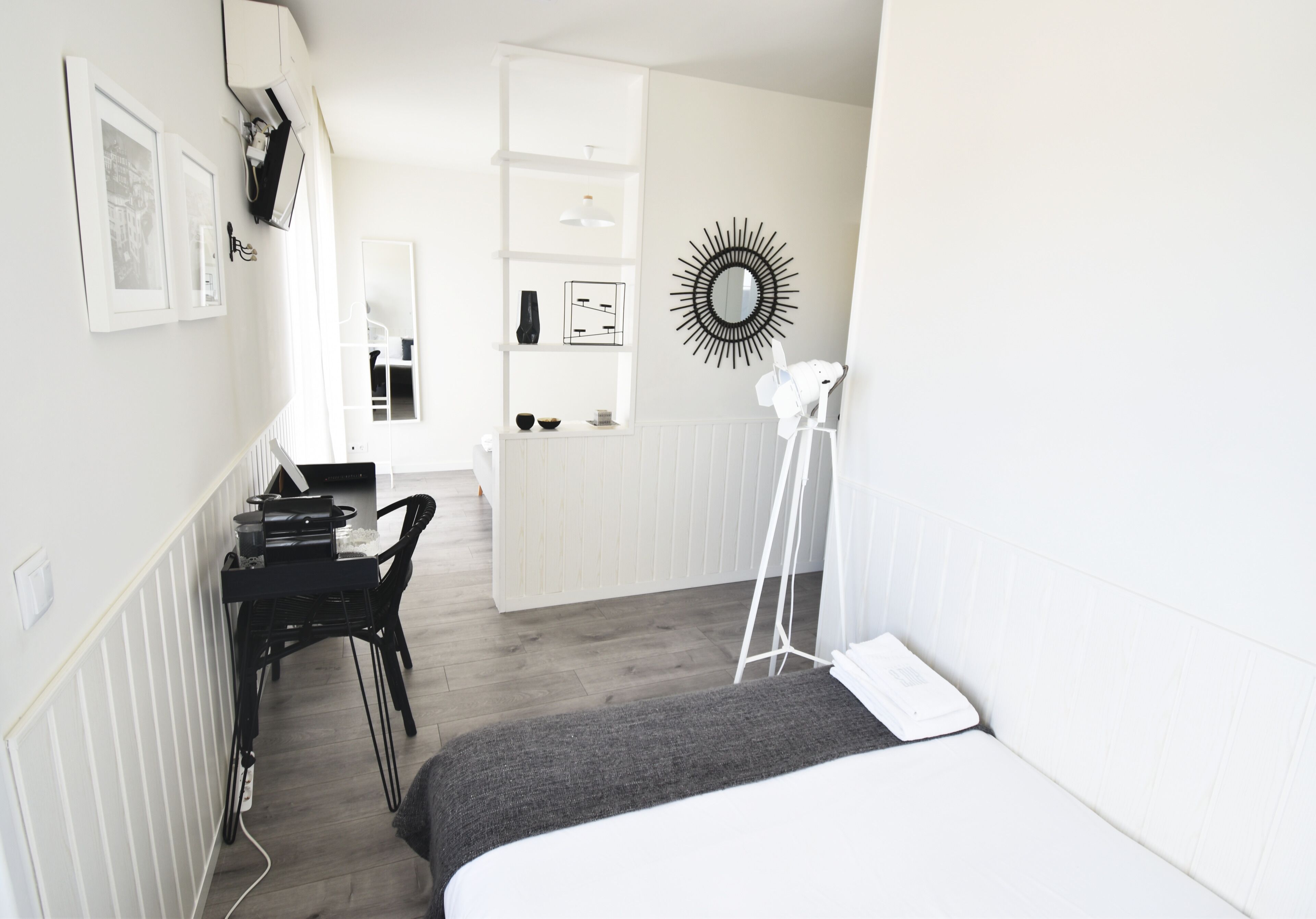 Ein modernes Schlafzimmer mit Bett, Schreibtisch und Stuhl. Ein weißer Kleiderschrank und ein Spiegel sind an der Wand angebracht.