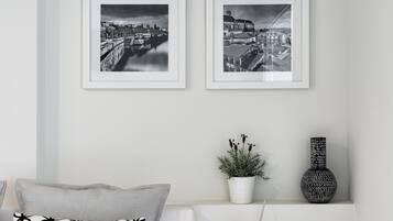 Ein Schlafzimmer mit einem Bett, zwei gerahmten Schwarz-Weiß-Stadtansichten an der Wand, einem weißen Nachttisch mit Lampe, einer Topfpflanze und einer dekorativen Vase.