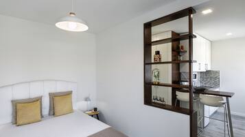A modern hotel room with a large bed, bedside table, lamp, and a view into the kitchen area.