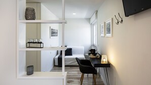 A modern, minimalist room with a bed, a desk, and a chair. There are shelves with decorative items and a TV mounted on the wall. - JR Studios & Suites (Coimbra)