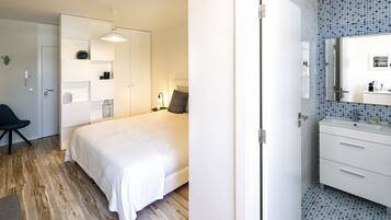 Ett modernt hotellrum med en säng, ett sängbord, en lampa och ett badrum med spegel och handfat.