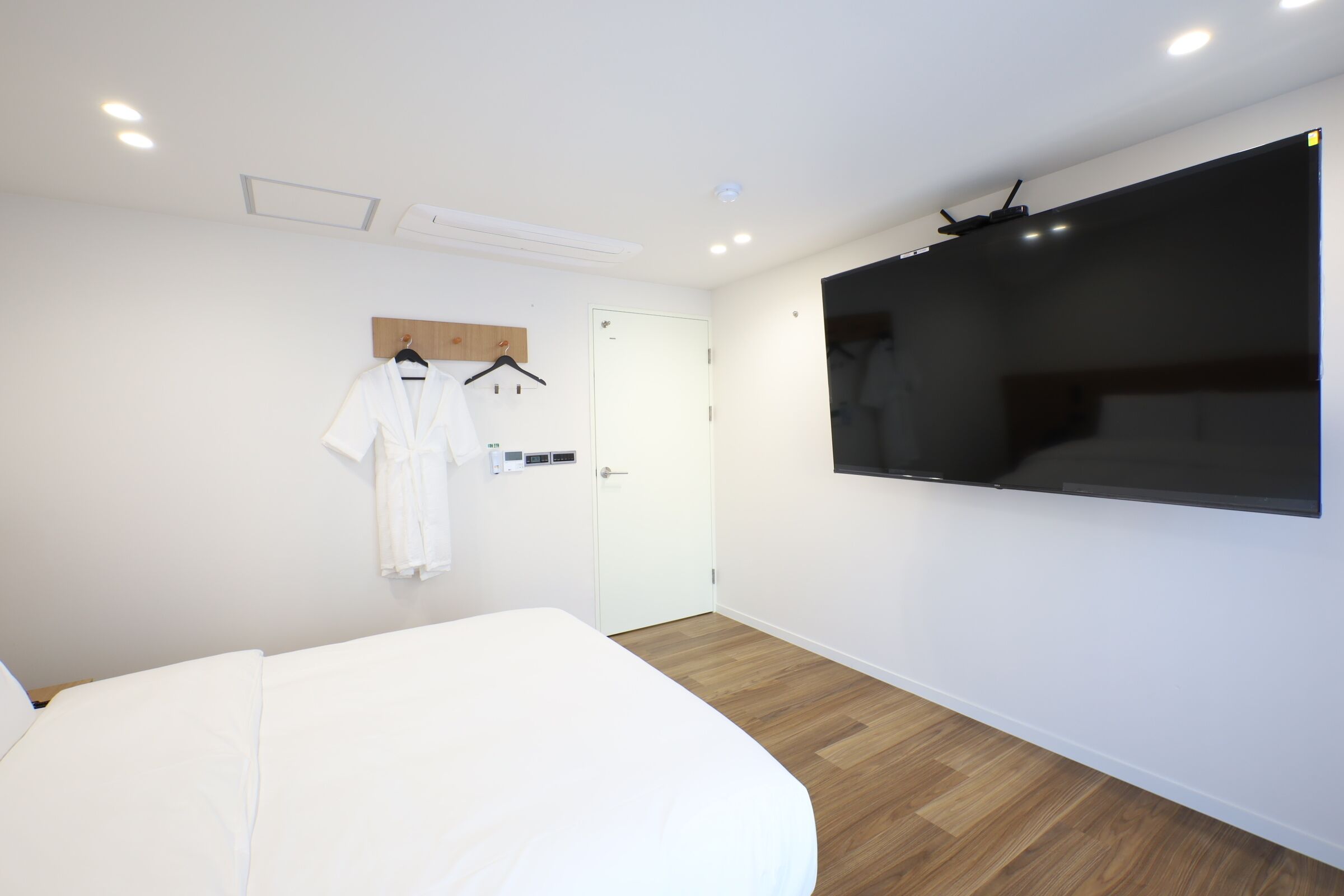 A modern hotel room with a large bed, a mounted TV, and a wooden floor.