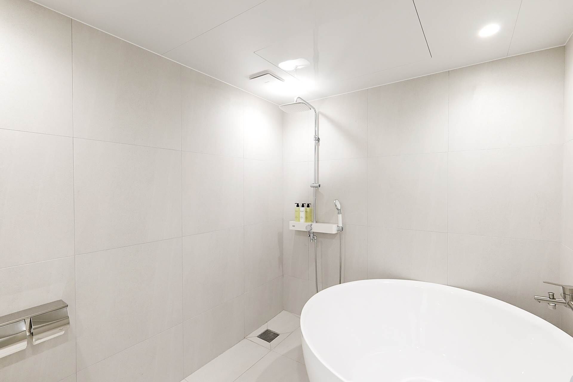 Een moderne badkamer met een vrijstaand bad, een douche met handdouche en een plank met toiletartikelen.
