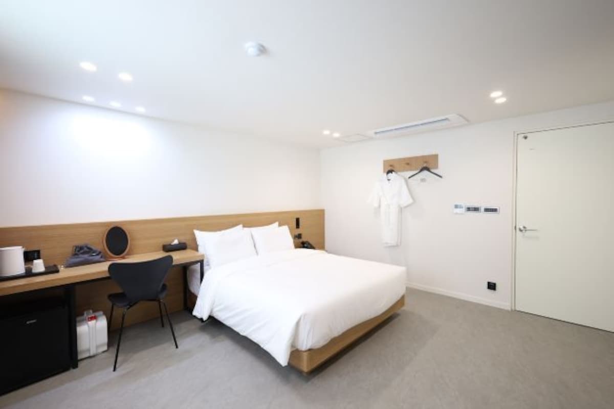 A modern hotel room with a bed, a desk, a chair, and a wardrobe.