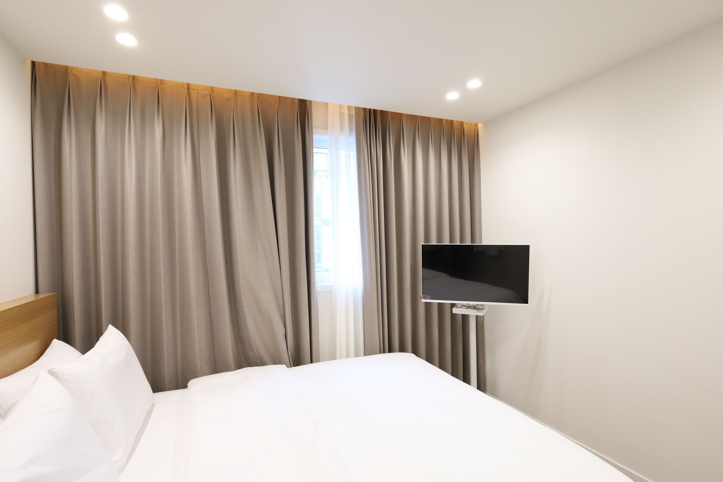 Een hotelkamer met een bed, gordijnen, een wandtelevisie en een raam.