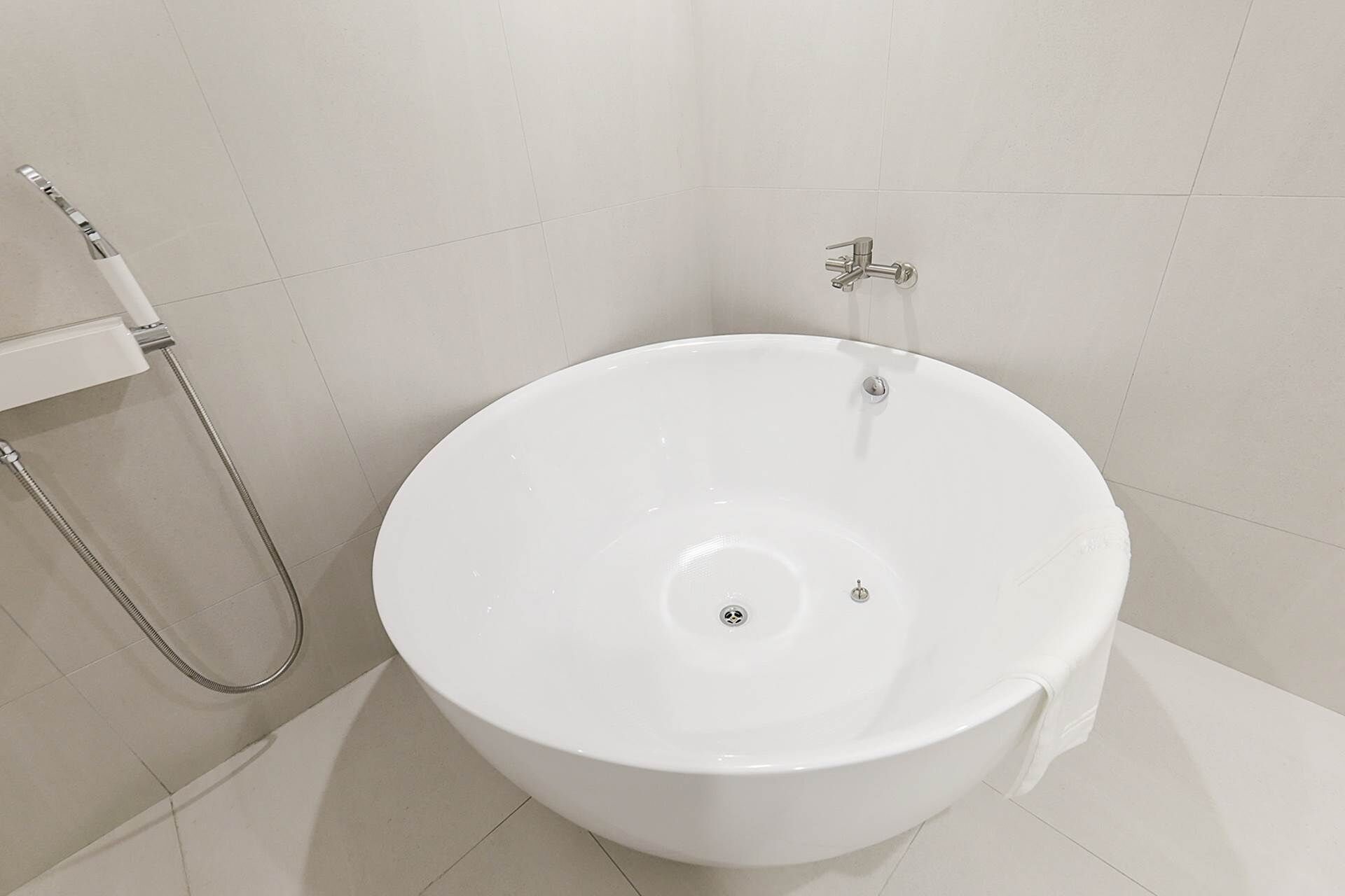 Un lavamanos pedestal blanco con un cabezal de ducha de mano en un baño con paredes de azulejos blancos.