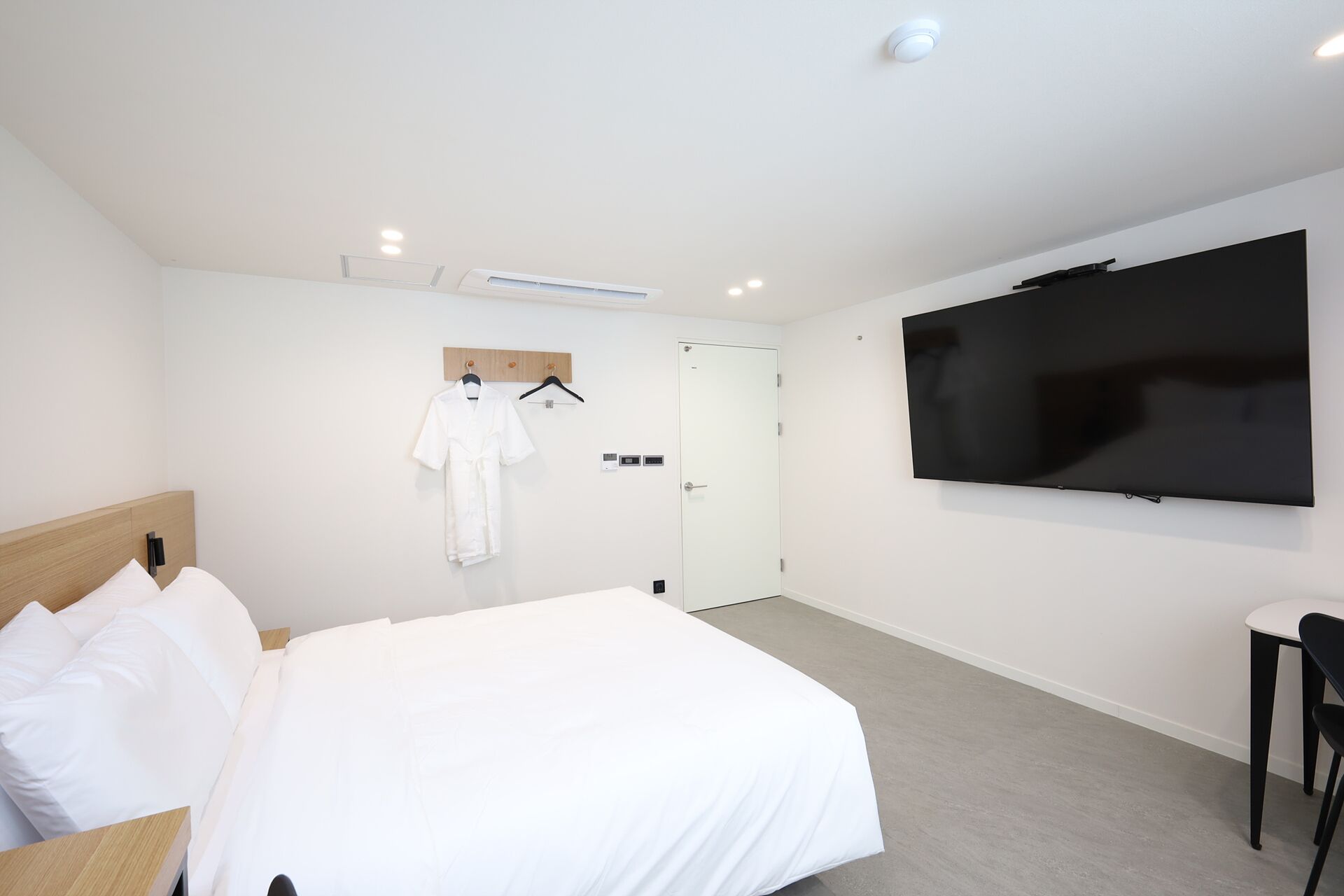 Una camera d'hotel con un letto, una televisione a muro, un accappatoio su un appendiabiti e una porta.