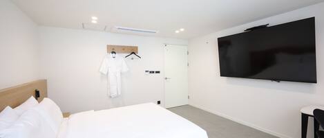 Una camera d'hotel con un letto, una televisione a muro, un accappatoio su un appendiabiti e una porta.