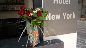 Ein Hotelschild mit der Aufschrift "Hotel New York" und eine farbenfrohe Vase mit roten Rosen und weißen Blüten davor.