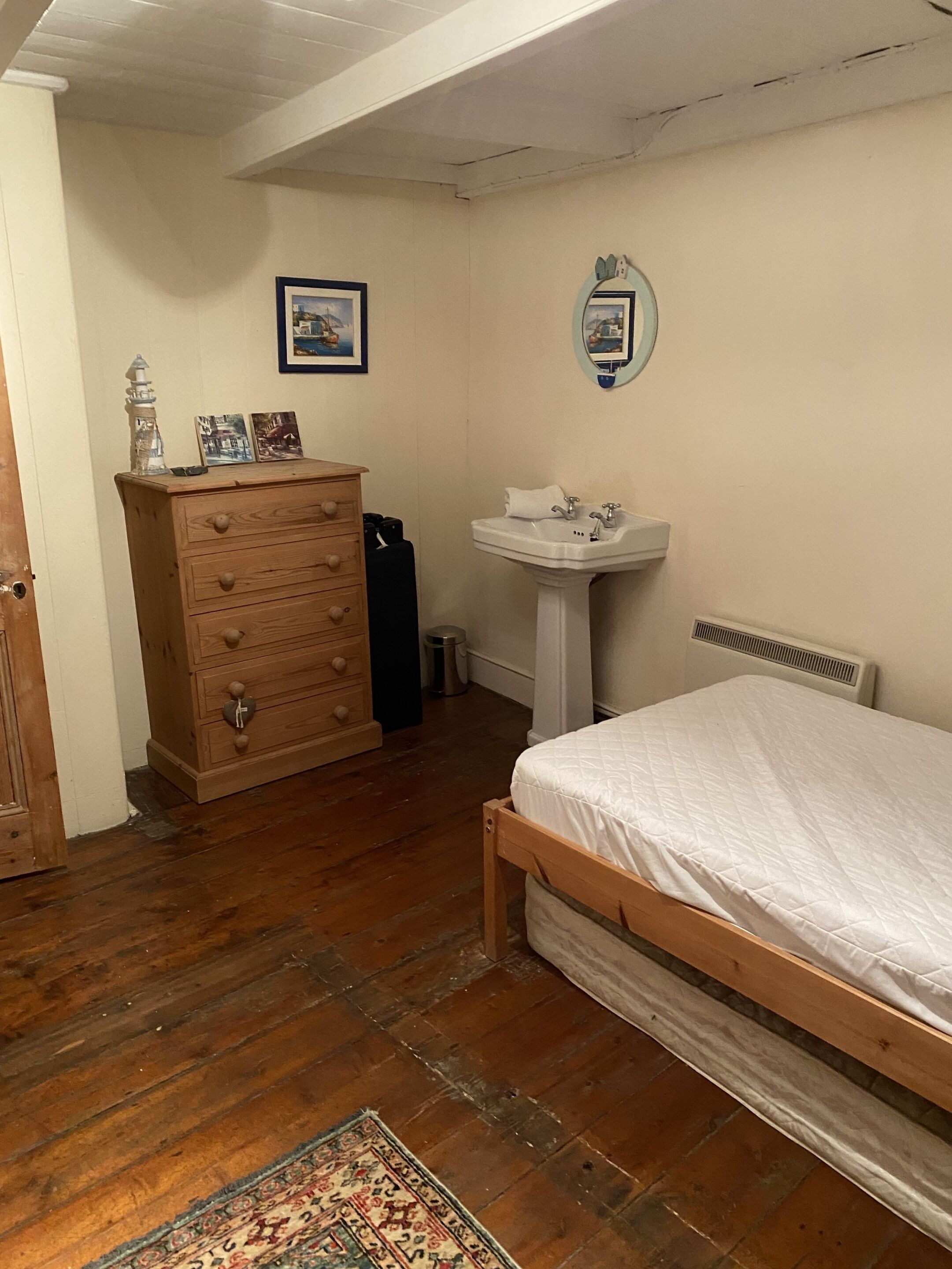 Un dormitorio con cama de madera, tocador, lavamanos blanco y un cuadro enmarcado en la pared.