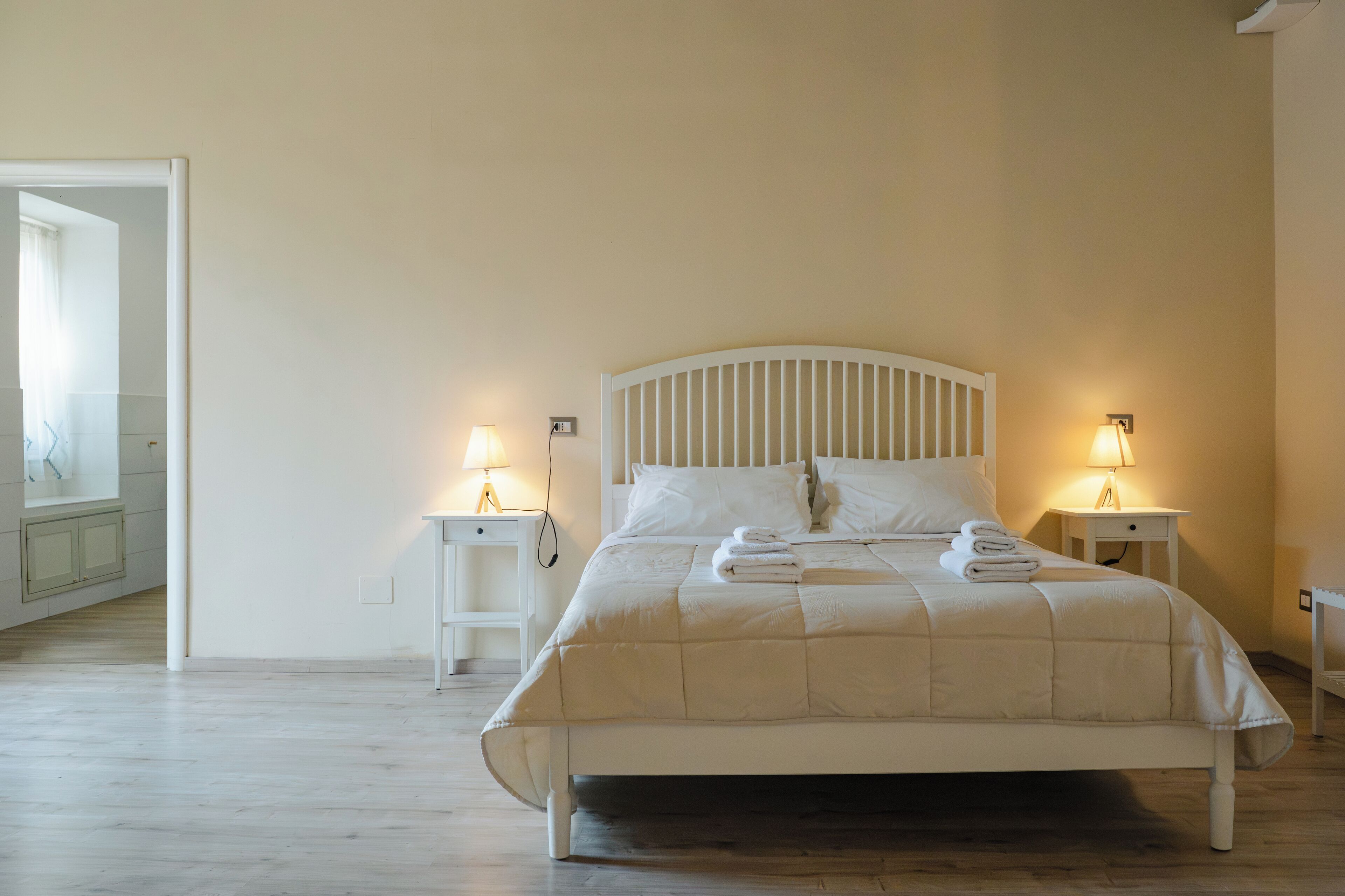 A neatly made bed with white bedding and pillows, two bedside tables with lamps, and a mirror on the wall.
