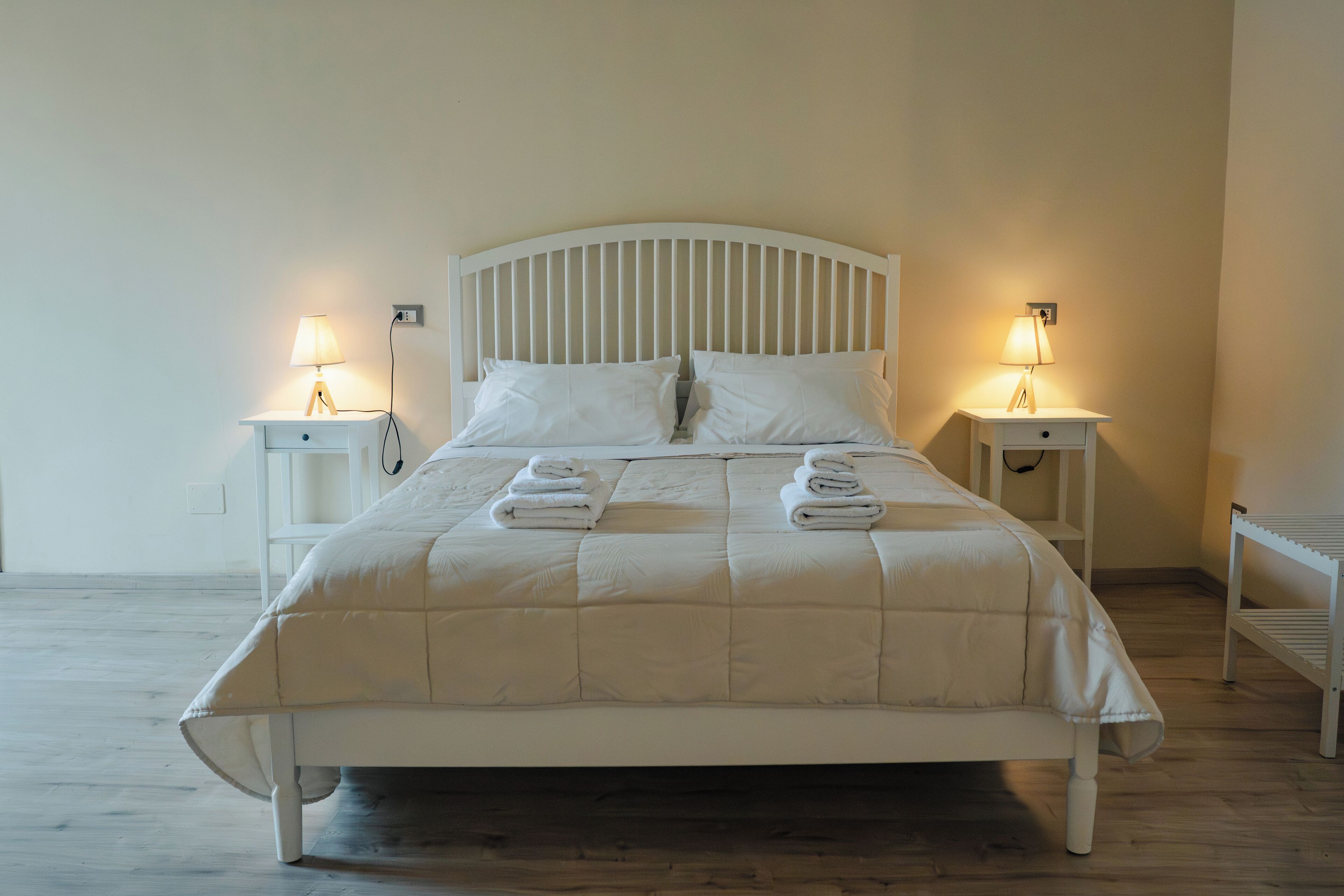 A neatly made bed with a white headboard and footboard, flanked by two bedside tables with lamps.