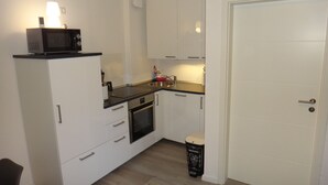 A compact kitchen with white cabinets, a microwave, a stove, and a small trash bin. - Ferienwohnung Hannah Hahnenklee (Goslar)