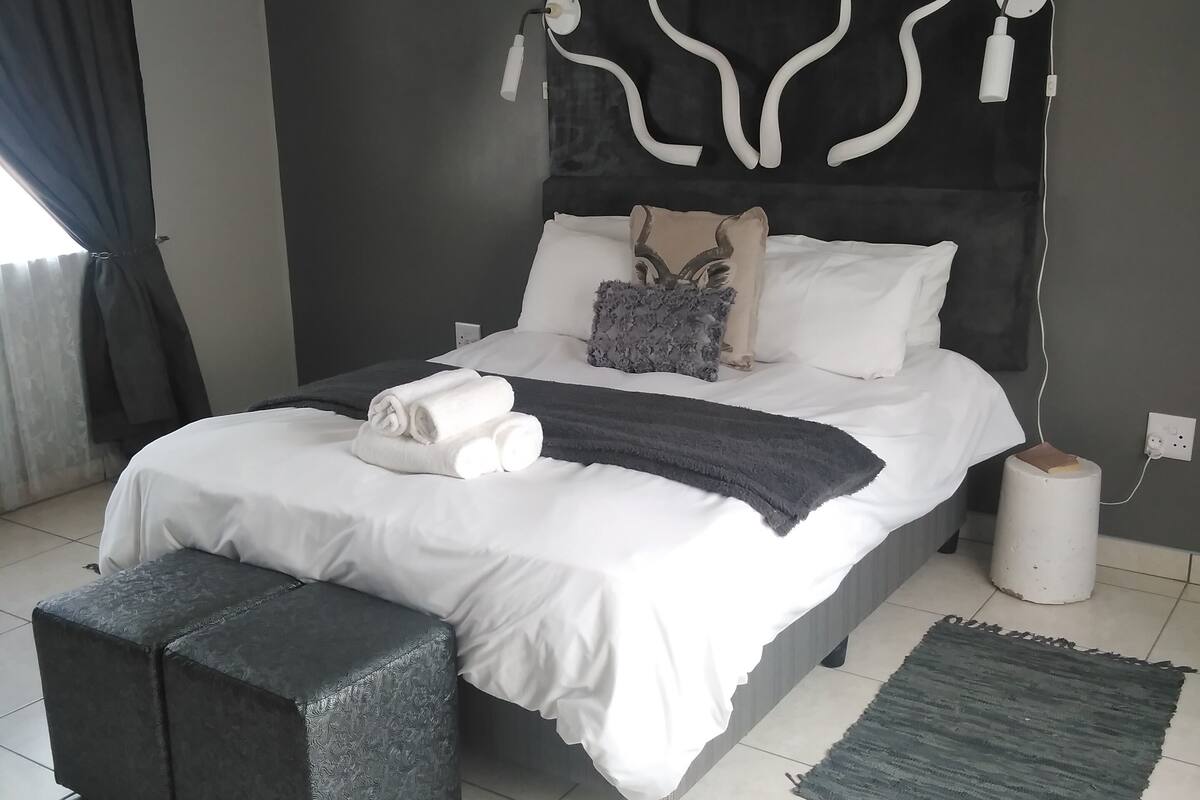 Un dormitorio moderno con una cama grande, una mesita de noche, una alfombra y una ventana con cortinas.