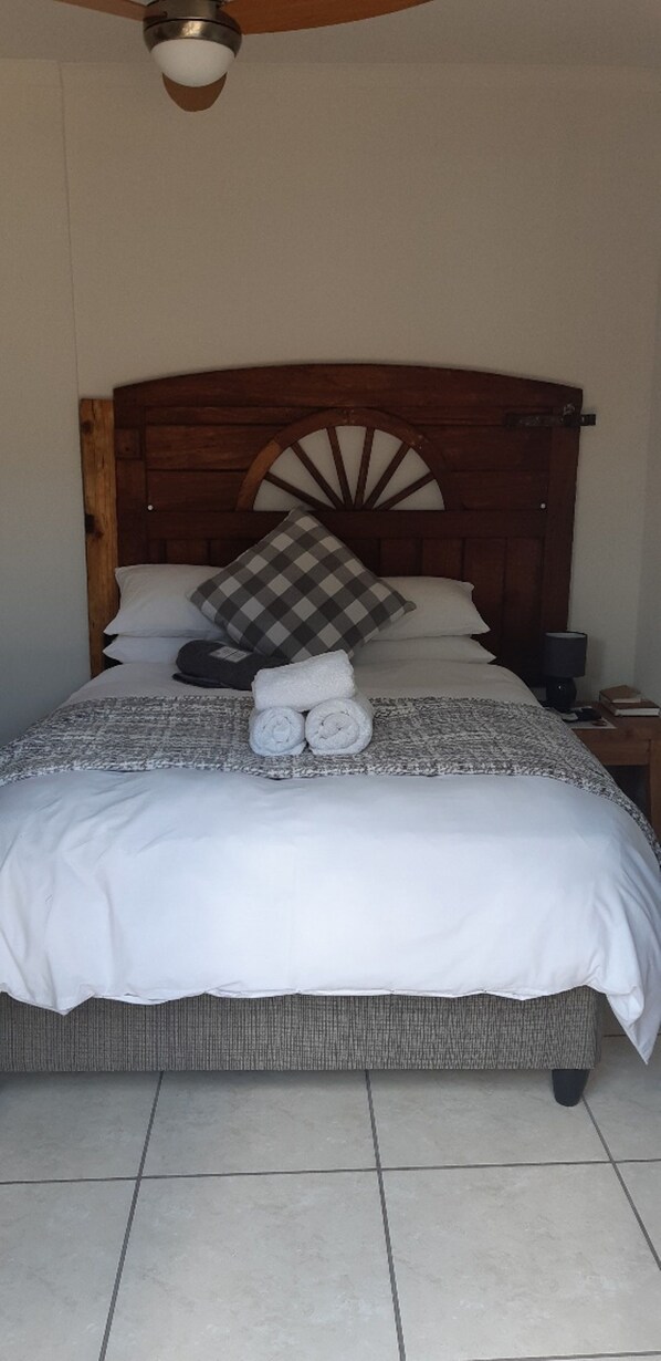 A neatly made bed with a wooden headboard, white bedding, and a checkered pillow.