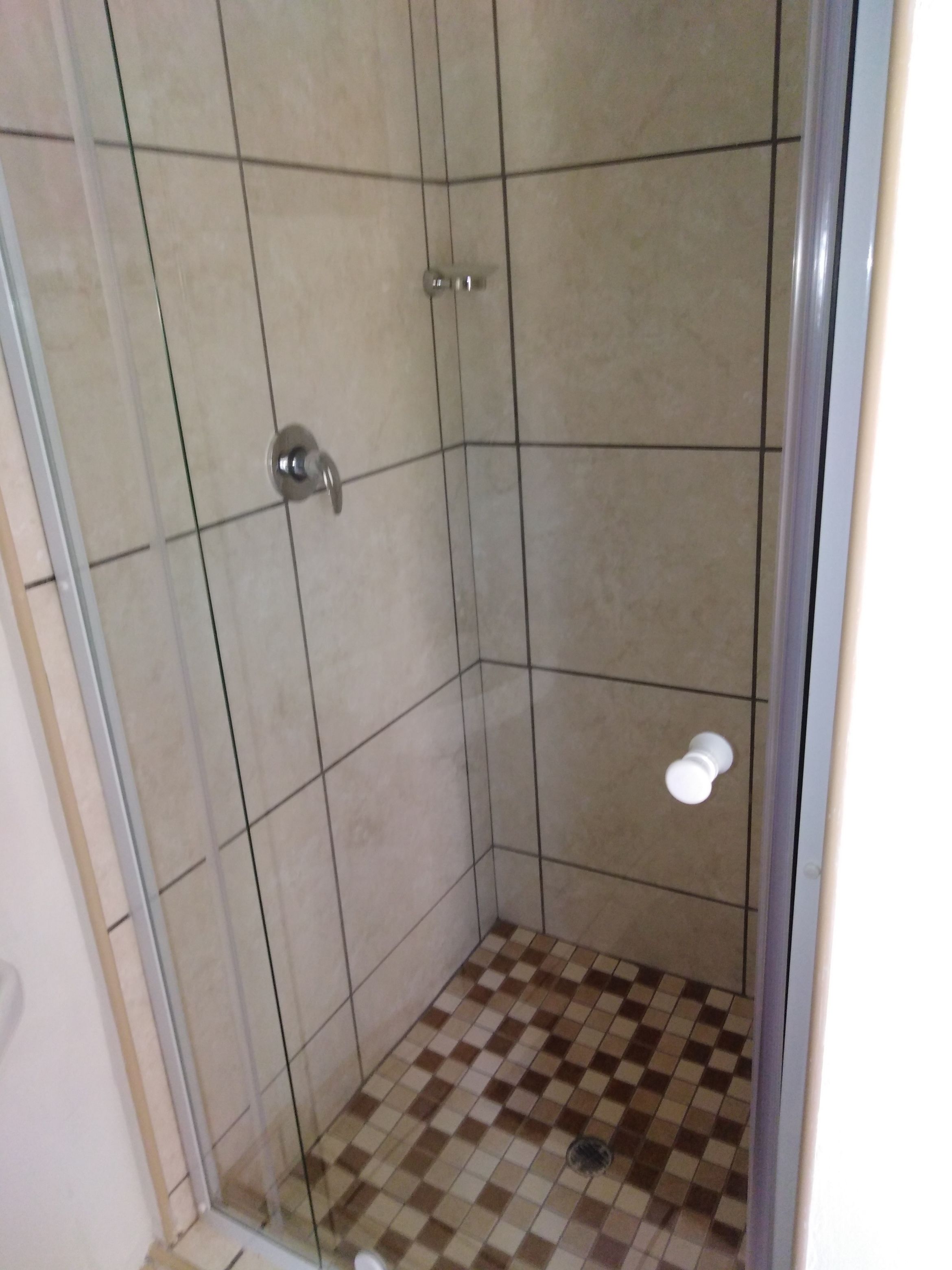 A shower with a glass door, tiled walls, and a checkered floor.
