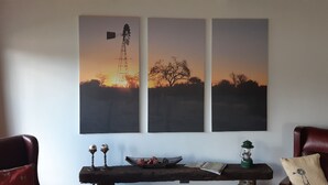 Una habitación con un cuadro grande colgado en la pared de un molino y árboles, una mesa de madera con objetos decorativos, y dos sillones de cuero.