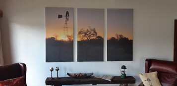 Una stanza con un grande quadro appeso al muro raffigurante un mulino a vento e alberi, un tavolo di legno con oggetti decorativi e due poltrone in pelle.