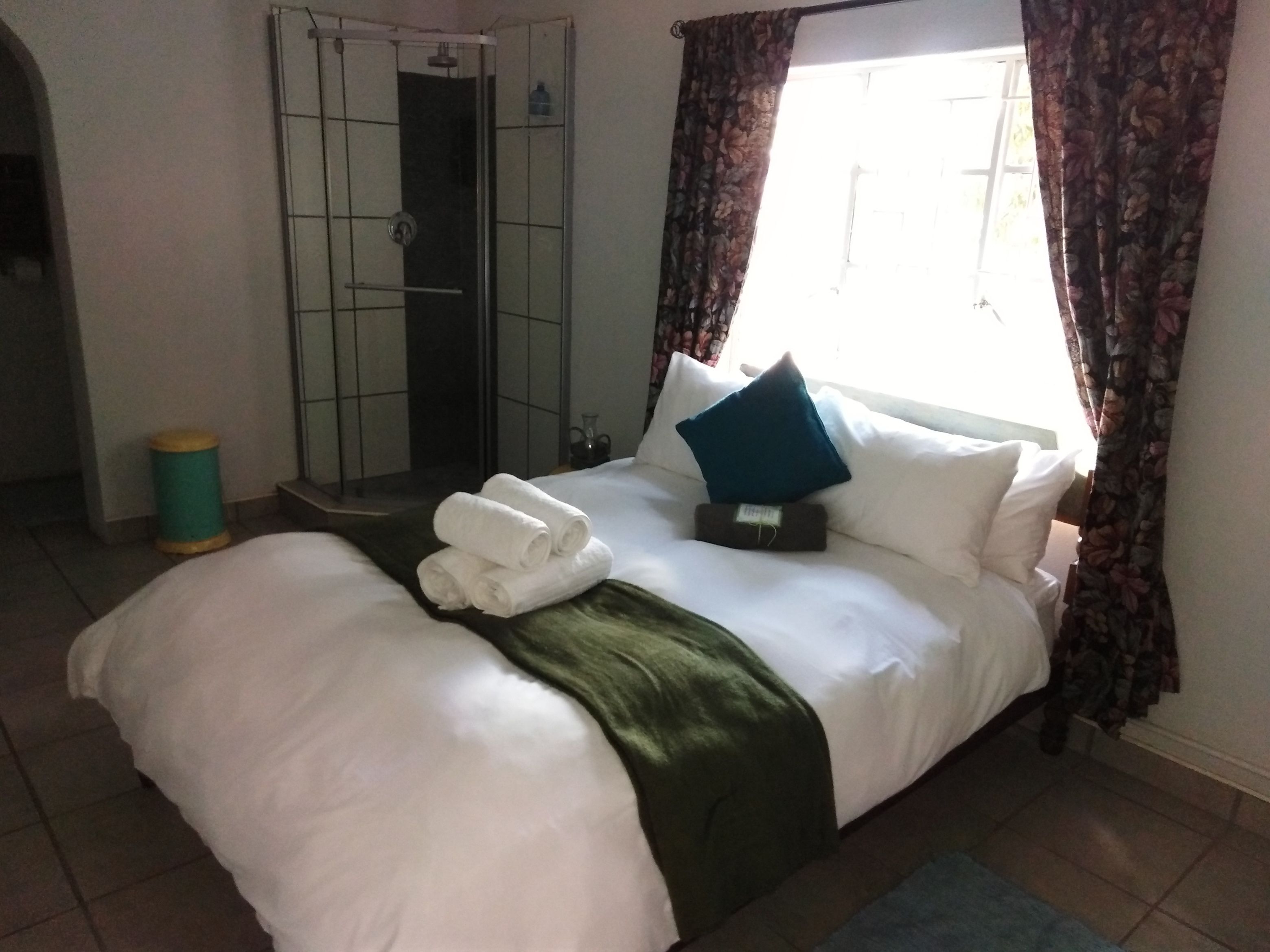 Hotellihuone, jossa on sänky, vihreä heittopeitto, sininen tyyny ja pyyhesetti.