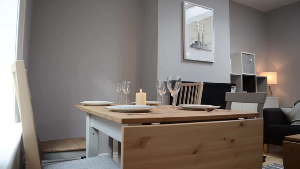 A dining area with a wooden table set for four, a chair, a framed picture on the wall, and a lamp on a side table. - Charming 2 Bedroom Cottage in Central Location (Dublin)