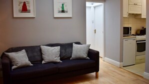 A dark-colored sofa with three pillows, a white door, and a kitchen area with cabinets and appliances. - Charming 2 Bedroom Cottage in Central Location (Dublin)