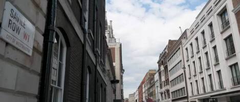 A street view with buildings, a sign for Savile Row W1, and parked cars.