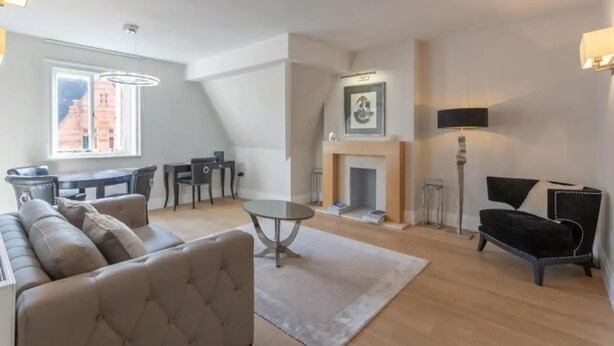 A living room with a sofa, a table, a fireplace, and a dining area. - Luxury Mayfair 2 Bedroom Apartment (London)