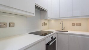 A modern kitchen with white cabinets, a black induction cooktop, and a stainless steel sink. - Luxury Mayfair 2 Bedroom Apartment (London)