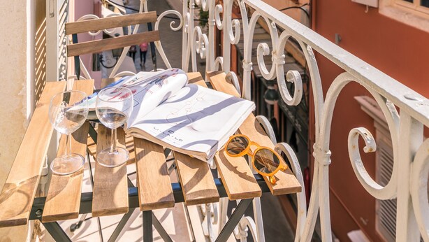Un balcón con una mesa, dos vasos y un par de gafas de sol. Se ve una torre del reloj al fondo.
