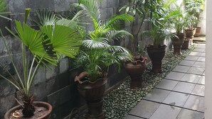 A corridor with a tiled floor, a stone wall, and potted plants along the wall. - Omahqu Guest House (Yogyakarta)