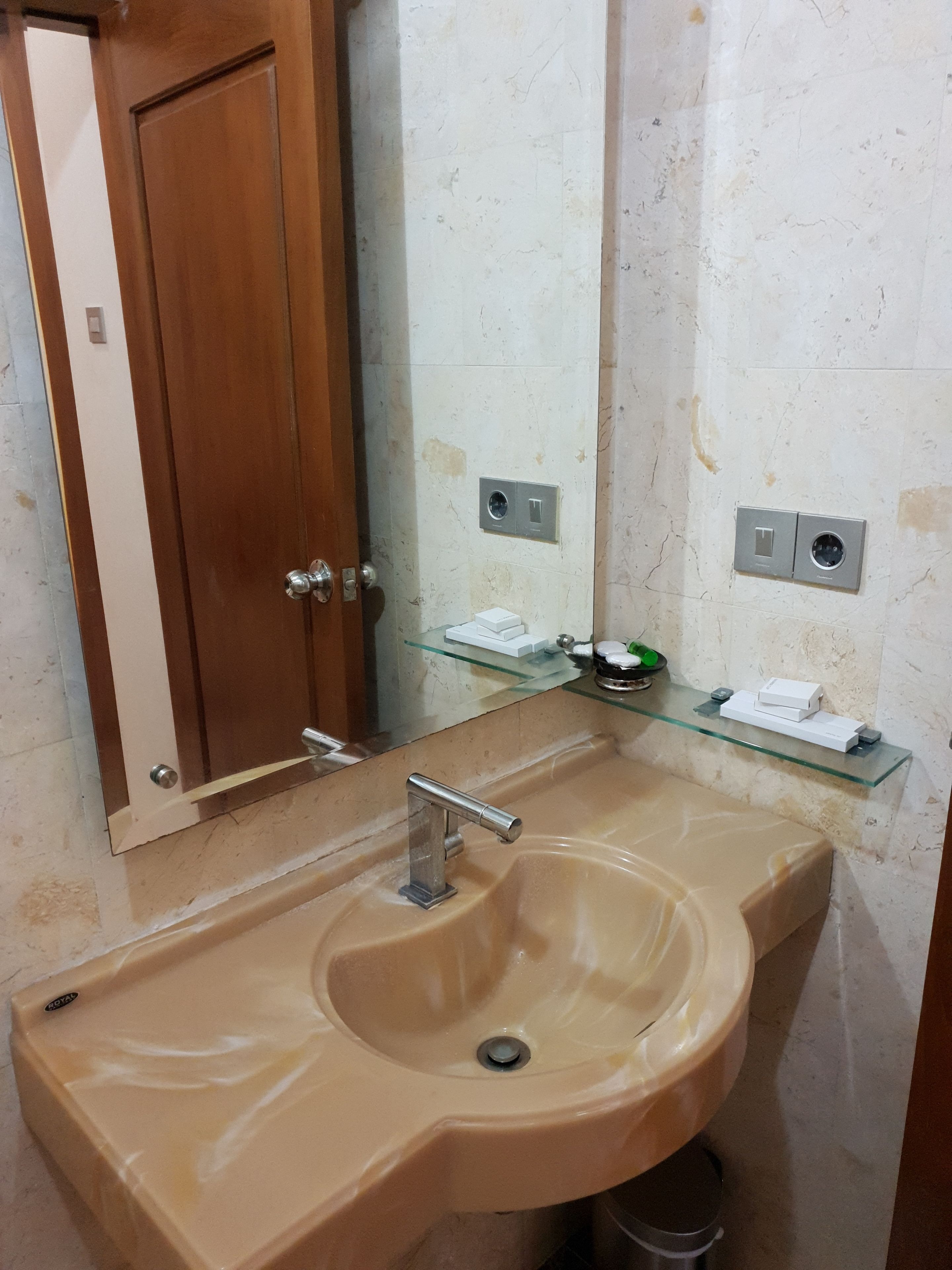 Een badkamer met een beige wastafel, een houten deur en een spiegel.