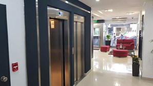 A modern lobby with a reception desk, two elevators, and a seating area with red chairs. - Palermo Bridge (Buenos Aires)