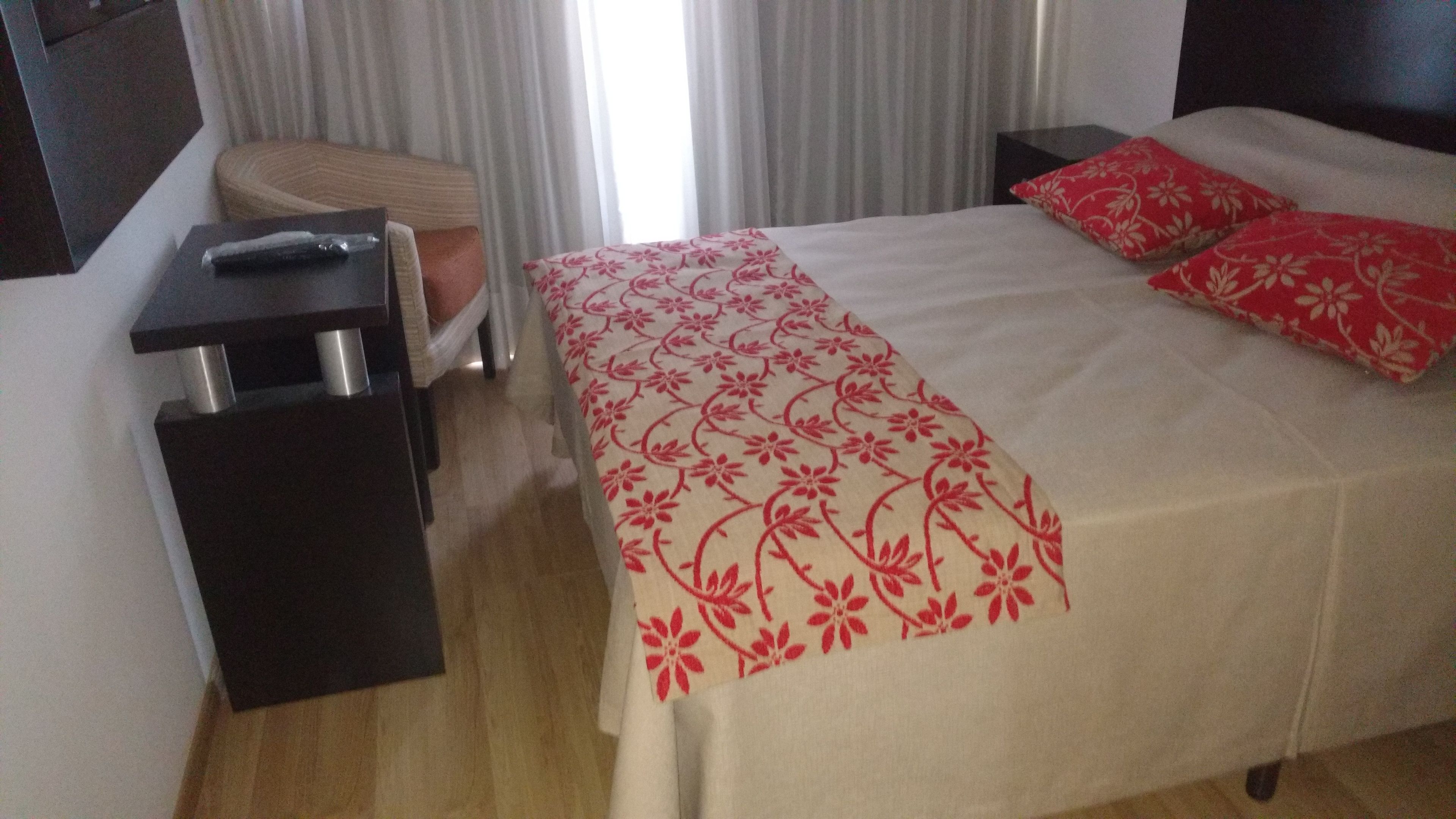 Una habitación de hotel con cama, mesita de noche, una silla y una ventana con cortinas.