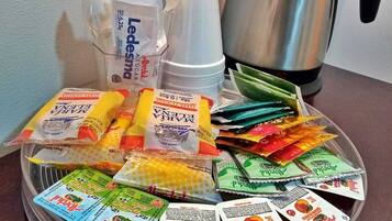 A tray with various food packets, a clear plastic cup, and a stainless steel coffee pot on a table.